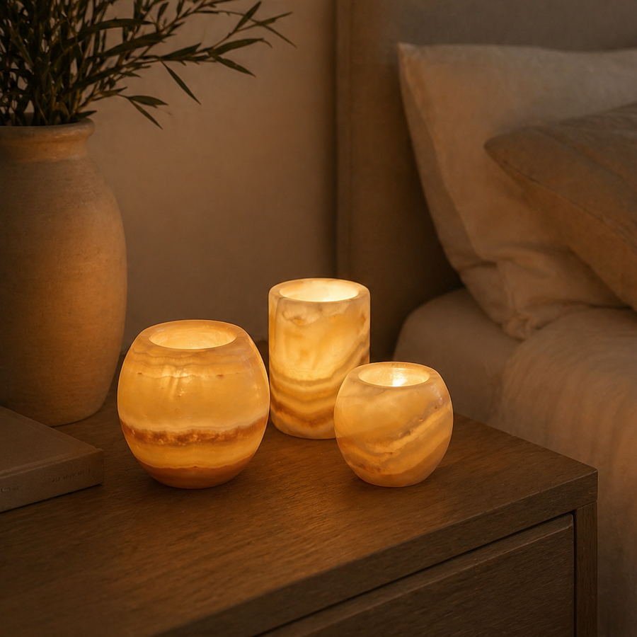 Three lit candles on a wooden surface next to a bed with pillows